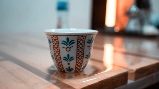 A patterned cup sits on a wooden table, with soft-focus background hinting at a domestic setting