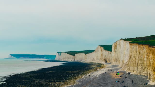 White chalk cliffs along a coastline with a pebble beach and a few people walking
