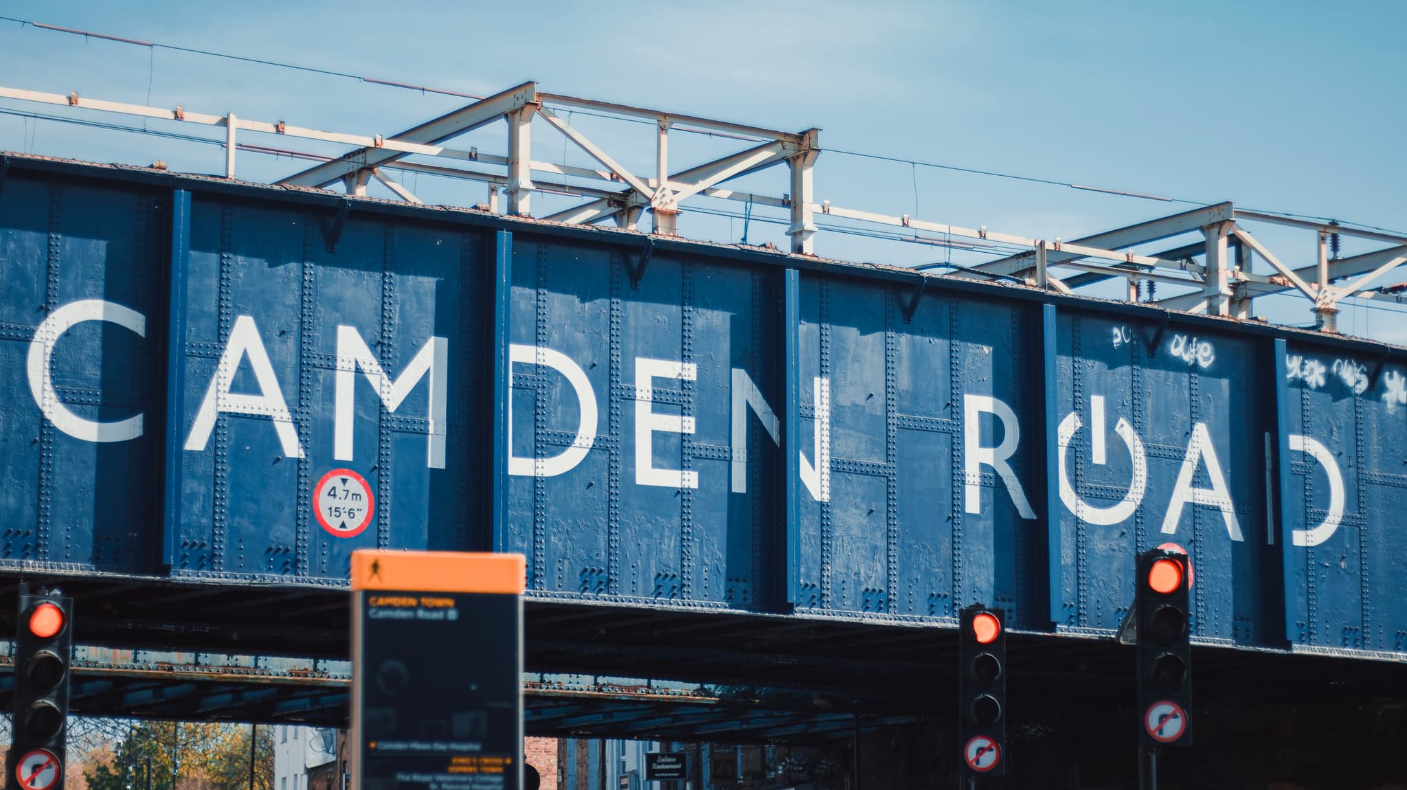 A bridge with the words CAMDEN ROAD painted on in large letters, likely indicating the name of the street or area, with a clear blue sky in the background