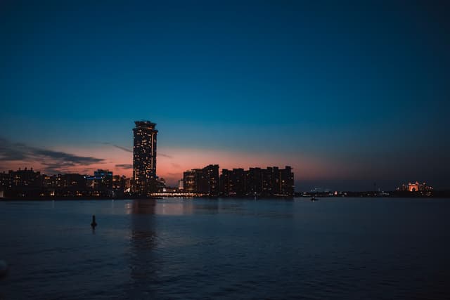 A twilight cityscape by a body of water, featuring a prominent building against a gradient sky fading from blue to orange