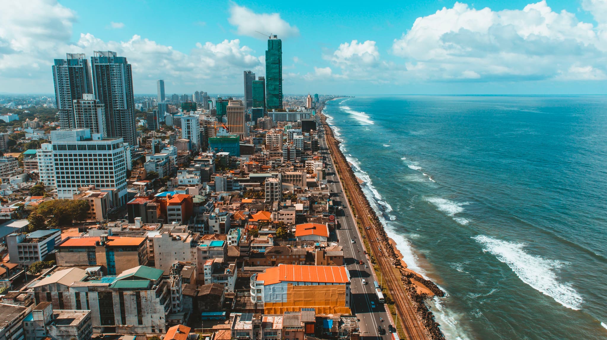 A coastal cityscape with high-rise buildings adjacent to a vast ocean, under a partly cloudy sky