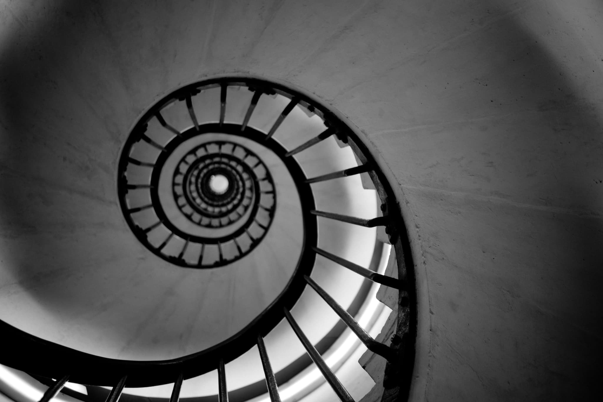 A black and white photo capturing the spiral architecture of a staircase from a low angle, emphasizing its symmetry and circular pattern