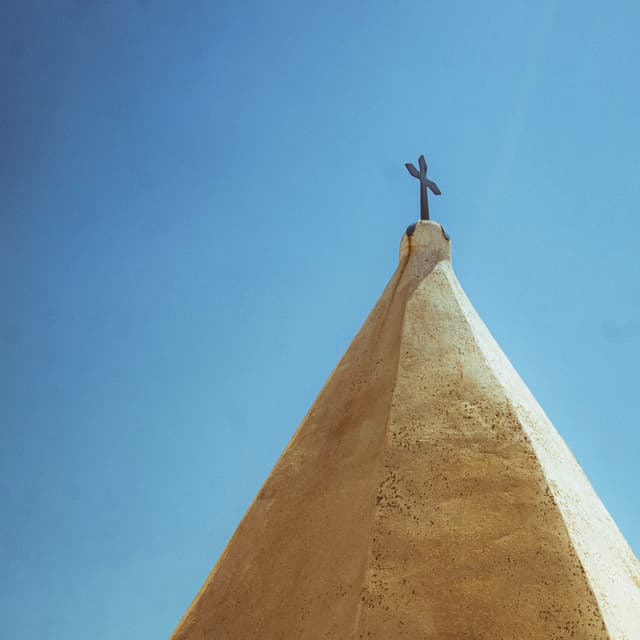 A tall, pointed structure with a cross on top against a clear blue sky