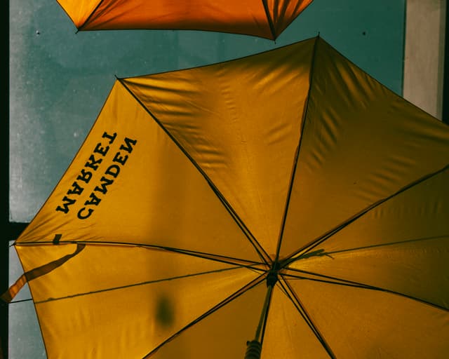 A yellow umbrella with text on it, slightly tilted, set against a blue background with geometric patterns