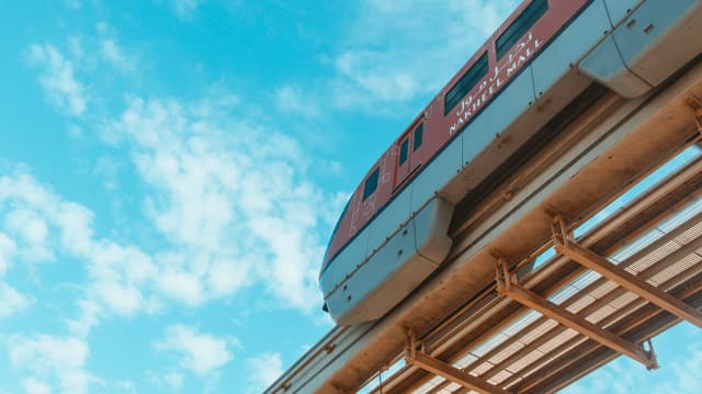 A train moving on an elevated track against a backdrop of a clear blue sky with fluffy clouds