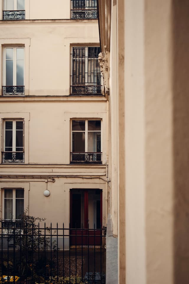 A narrow view between buildings, focusing on the facade of a multistory residential structure with balconies and windows, evoking an urban European charm