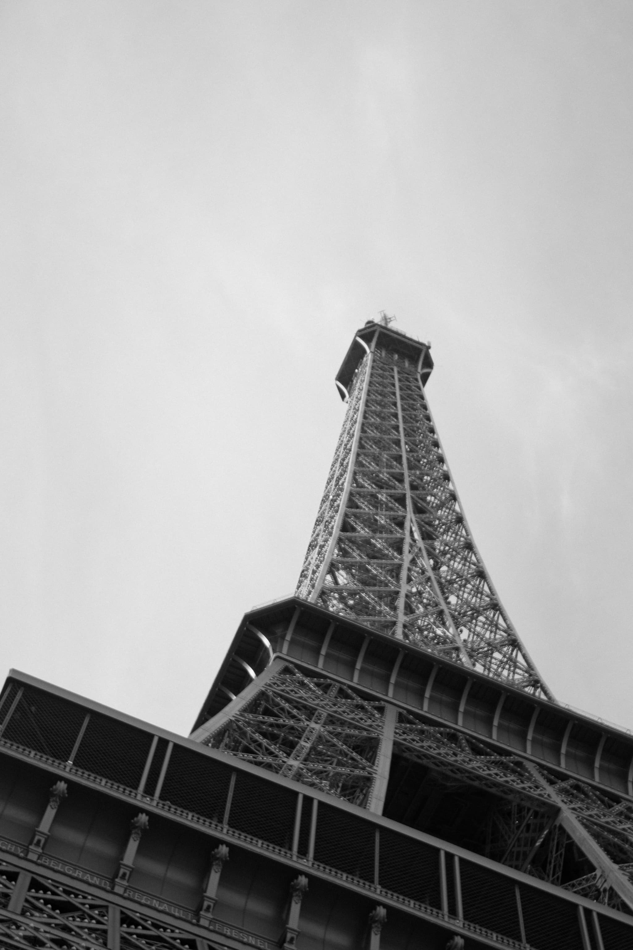 An upward-looking black and white view of the Eiffel Tower against a cloudy sky